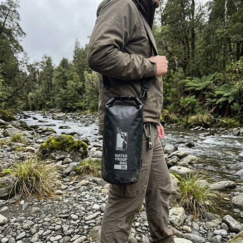 Bolsa seca Dukha 5L negra al hombro junto a un río
